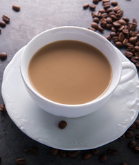  White cup of coffee with milk or tea with milk on dark grey beton background decorated with coffee beans. Copy space