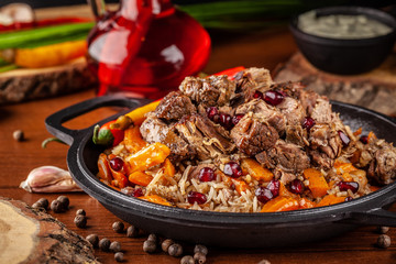 Uzbek traditional cuisine. Pilaf or plov with lamb, and red garnet, in an iron cast-iron frying pan kazan. Background image. Copy space, selective focus - obrazy, fototapety, plakaty