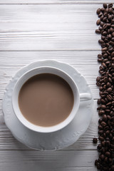   White cup of coffee with milk or tea with milk on white wooden background decorated with coffee beans. Copy space
