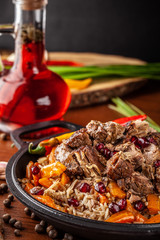 Uzbek traditional cuisine. Pilaf or plov with lamb, and red garnet, in an iron cast-iron frying pan kazan. Background image. Copy space, selective focus