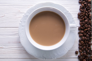   White cup of coffee with milk or tea with milk on white wooden background decorated with coffee beans. Copy space