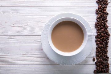   White cup of coffee with milk or tea with milk on white wooden background decorated with coffee beans. Copy space