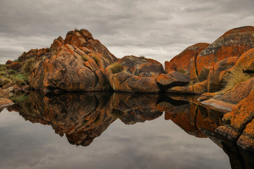 The black water in this rock pool is cold and uninviting but with barely a ripple, it makes for a nice mirror-like surface to reflect the red lichen covered granite rocks.