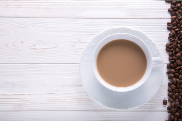   White cup of coffee with milk or tea with milk on white wooden background decorated with coffee beans. Copy space