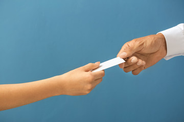 Man giving business card to woman on color background