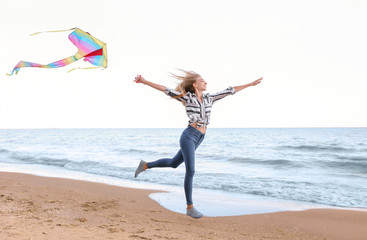 Obraz premium Beautiful young woman flying kite near sea