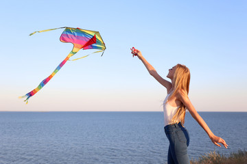 Beautiful young woman flying kite outdoors