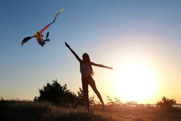 Beautiful young woman flying kite outdoors at sunset