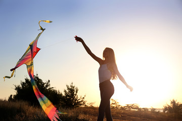 Beautiful young woman flying kite outdoors at sunset