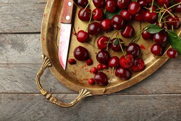 Metal tray with ripe cherries on wooden table