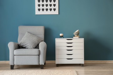 Stylish interior of living room with comfortable armchair and commode near color wall