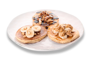 Plate with tasty pancakes, walnuts and sliced banana on white background