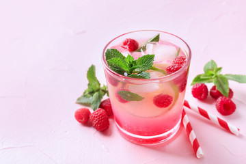 Glass of fresh raspberry mojito on color background