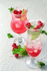 Glasses of fresh raspberry mojito on white textured background