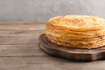 Wooden board with stack of tasty thin pancakes on table