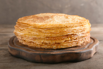 Wooden board with stack of tasty thin pancakes on table