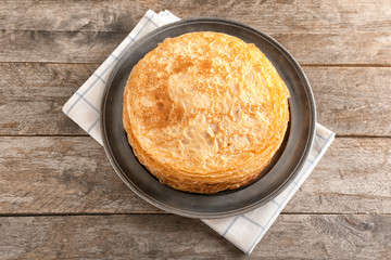 Plate with stack of tasty thin pancakes on wooden table