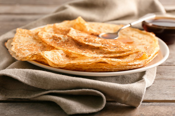 Plate with tasty thin pancakes on wooden table