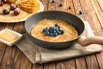 Frying pan with delicious thin pancakes and berries on wooden table