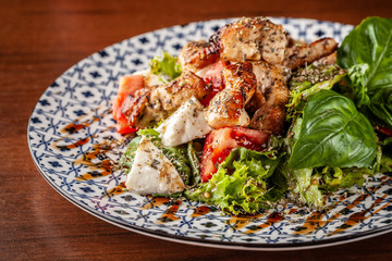 Uzbek traditional cuisine. Salad Zarafshon from roasted chicken fillet, mozzarella cheese, tomatoes, lettuce leaves, olive oil, mustard sauce. Background image. Copy space, selective focus