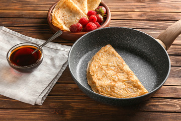 Frying pan with delicious thin pancakes and syrup on wooden table