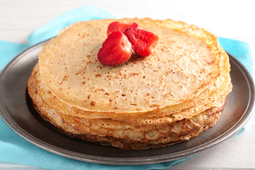 Stack of delicious thin pancakes with strawberries on plate