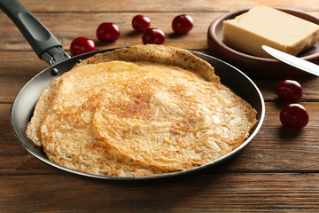 Frying pan with delicious thin pancakes on wooden table