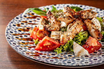 Uzbek traditional cuisine. Salad Zarafshon from roasted chicken fillet, mozzarella cheese, tomatoes, lettuce leaves, olive oil, mustard sauce. Background image. Copy space, selective focus