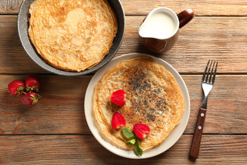 Delicious thin pancakes with berries and milk on wooden table