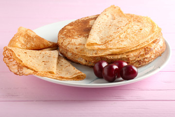 Plate with delicious thin pancakes and sweet cherries on wooden table