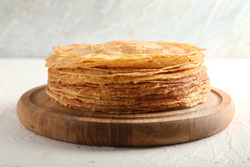 Stack of delicious thin pancakes on wooden board