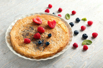 Plate with delicious thin pancakes and berries on wooden table