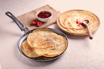 Delicious thin pancakes with strawberry jam on table