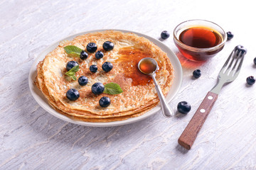 Plate with delicious thin pancakes, berries and syrup on wooden table
