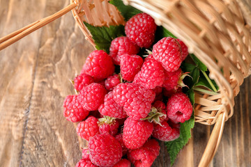 Wicker basket with scattered raspberries on wooden background