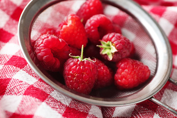 Sieve with ripe aromatic raspberries on napkin, closeup