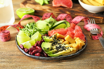 Plate with delicious fresh salad and measuring tape on table. Diet concept