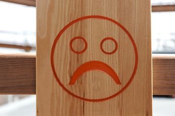Red unhappy smiley on brown wooden background