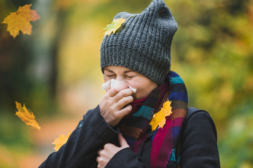 Woman sneezes and blows his nose in a handkerchief in an autumn park