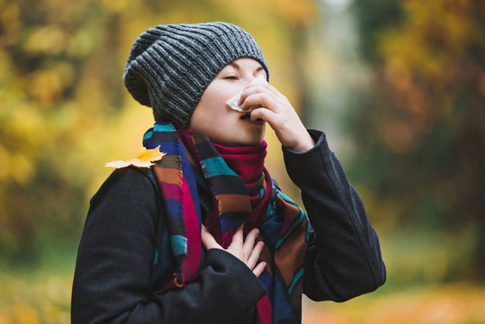 Woman sneezes and blows his nose in a handkerchief in an autumn park