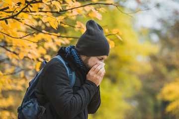 man sneezes and blows his nose in a handkerchief in an autumn park