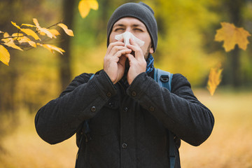 man sneezes and blows his nose in a handkerchief in an autumn park