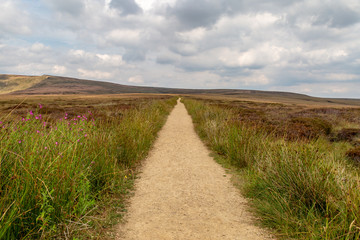 Fototapeta na wymiar Looking down an empty pathway along the Pennine Way in Derbyshire, with a cloudy sky overhead