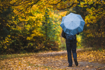Man under blue umbrella walks in the park in autumn