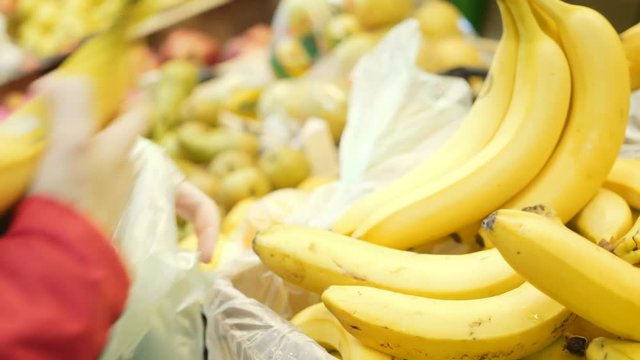 A woman in a red jacket buys bananas in a supermarket.