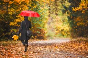 Woman under red umbrella walks in the park in autumn