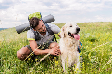 Traveler with backpack and dog sitting on green meadow