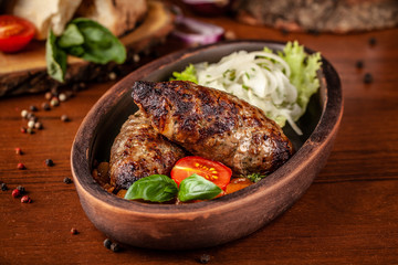 Uzbek traditional oriental cuisine. Lulya kebab from ground beef with pickled onion, salad, cherry tomatoes in a dish of red clay. Background image. Copy space, selective focus