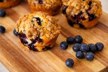 freshly baked blueberry muffins with an oat crumble topping on a natural wooden board