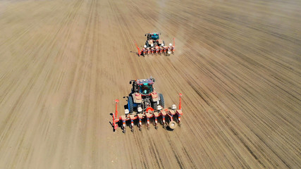 Naklejka premium Aerial view of a farmers in two tractors seeding, sowing agricultural crops at field